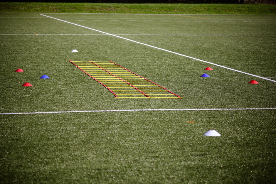 Agility ladder and marker cones set up on a grassy football field for training.